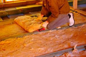 A worker adding batt insulation to a floor.