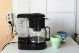 a coffee maker with two cups next to it on the counter