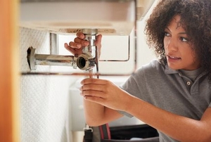 woman fixing pipe under sink