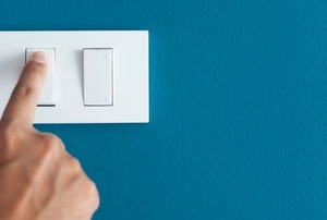hand pressing light switch on bright teal wall