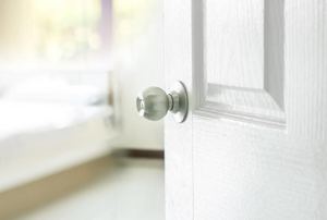 A white door with a silver knob opens into a brightly lit room.