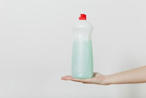 A hand holding a bottle of dish soap against a white background to be used for killing weeds.