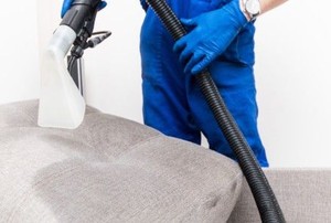 a person with gloves cleaning a couch cushion with a vacuum cleaner