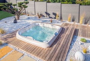 hot tub in wooden deck with stone and grass landscaping