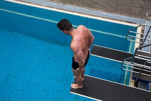 man standing on a diving board looking into a pool below