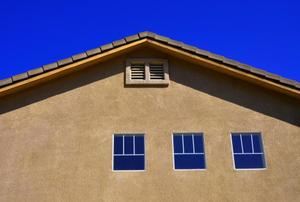 A gable vent and three windows on a stucco house.