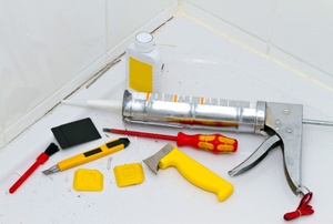 A caulk gun and caulking supplies laying on the floor of a shower.