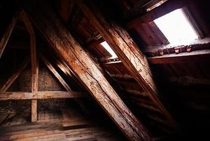The corner of a dimly-lit old attic with two small windows on the near wall.