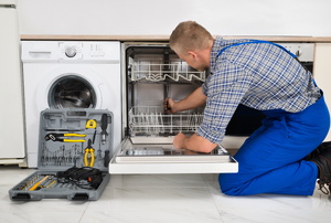 A repair man servicing a dishwasher.