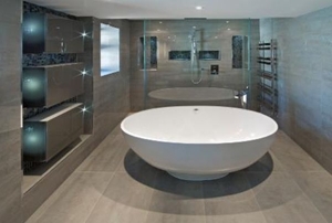 A white oval shaped bath tub in an expensive new home in an ultra modern bathroom.