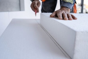 hands measuring thick sheet of foam board insulation
