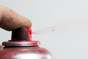 A finger holding down the nozzle of a bottle with red spray paint.