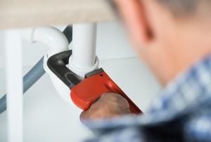 A man using a pipe wrench underneath a sink.