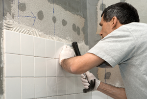 man installing white tile on the wall of a shower