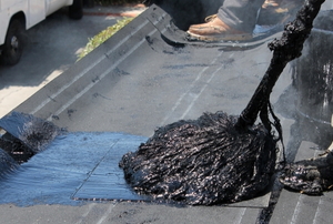 applying hot roofing tar with a mop