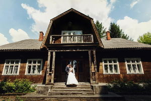 A bride and groom posing in front of a rustic farmhouse. 