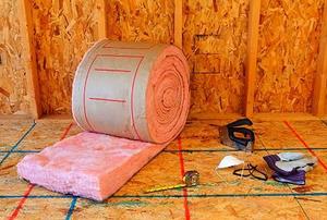 A roll of pink, fiberglass insulation with attendant tools in front of an unfinished wall.
