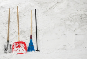 A set of snow removal tools, including a shovel and broom, against a snowy background. 