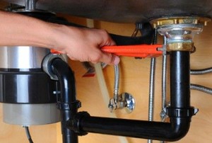 hand with wrench adjusting plumbing beneath a sink