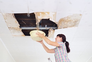Woman with bucket under leaking ceiling