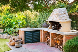 A small outdoor kitchen with a wood-burning oven surrounded by plants.