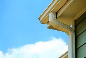 A from-under view of a soffit, gutter, and drain pipe on the corner of a house.