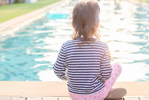 A young girl sits by a sunny pool.