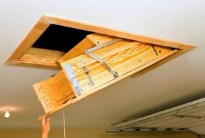A hand pulling down a folding access ladder.