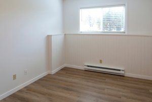 A white baseboard heater in a room with a hardwood floor.