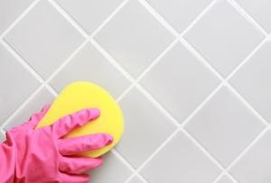A gloved hand cleaning a shower wall with a sponge.