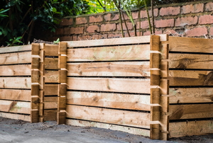 large wooden compost bins by a brick wall