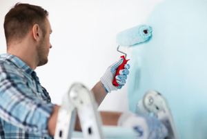 A man paints a room being painted light blue.