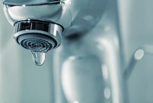 A silver faucet with water dripping from it and the potential for lead in the drinking water.