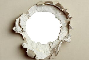 A round hole in wall with drywall peeling. 