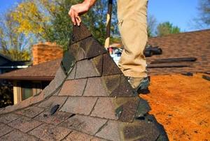 A worker lifting up a layer of shingles on a roof.