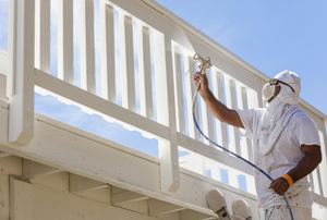 A painter using an electric spray painter to cover a deck railing.
