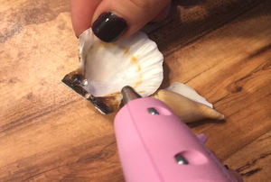 A pink hot glue gun being used to glue small seashells.