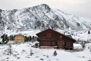 A vacant summer hosts sits in snow with mountains in the background.