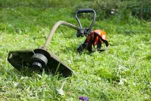 A weed eater lying on the grass, unused.
