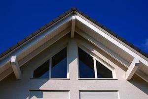 Exterior view of attic-gable windows on a white house with a pitched roof.