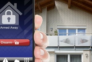 A smart phone held in front of a house with a security app on the screen.