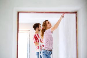 A young couple painting the inside of a house. 