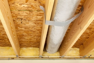 A plywood floor from underneath with a silver duct.