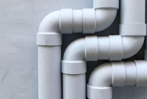 three sets of white PVC pipes against a gray wall