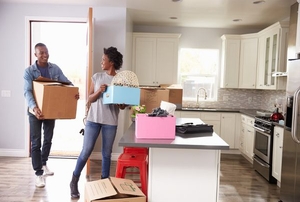 A young couple moving boxes into a kitchen.