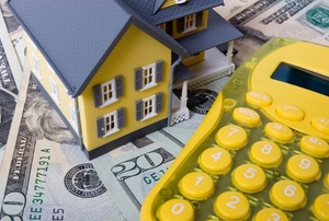 A yellow calculator with cash and a small plastic house.