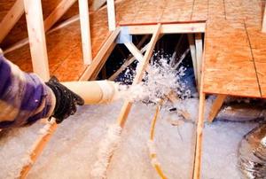 A tube spraying blown-in insulation into the space below an attic floor.