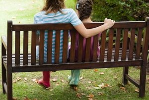 a woman and girl sitting on a garden bench