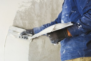 A man applying white putty to a wall.