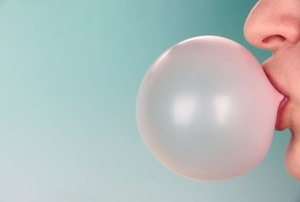 A person blowing a bubble in chewing gum against a blue background.